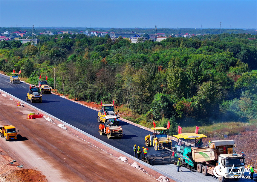 工人在加緊鋪設瀝青路面，一片繁忙施工景象。人民網 朱海鵬攝