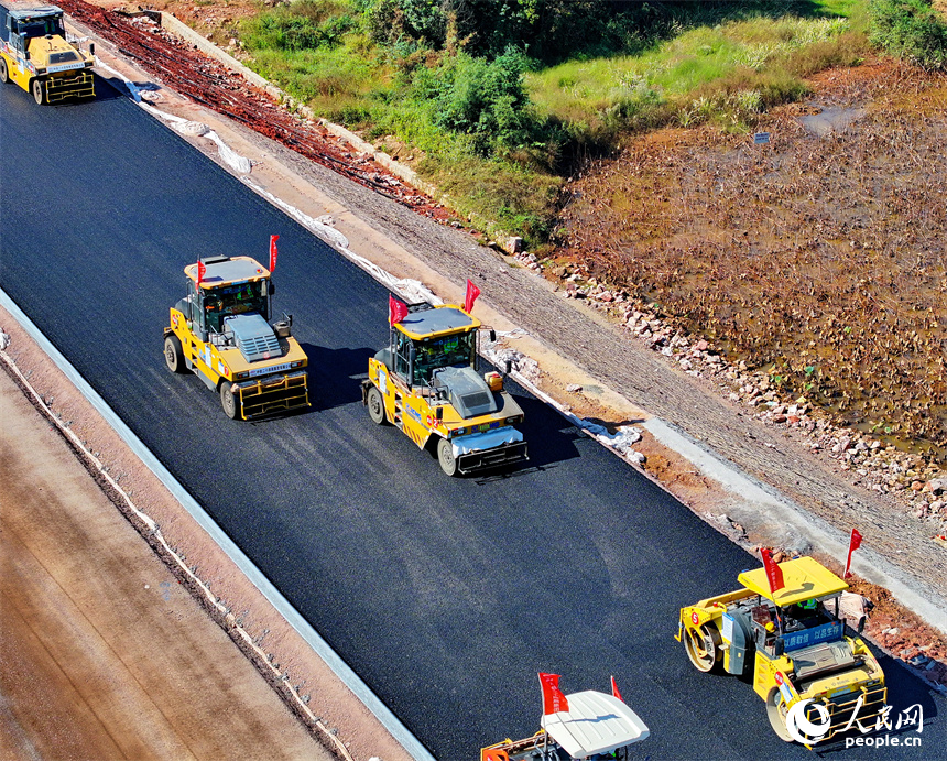 工人在加緊鋪設瀝青路面，一片繁忙施工景象。人民網 朱海鵬攝