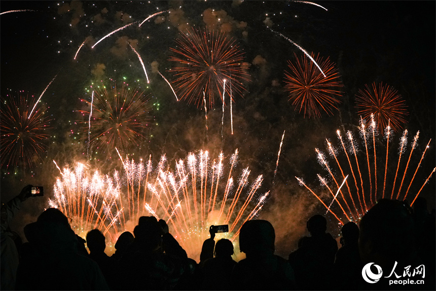 煙花在夜空中綻放，人群在光影間交錯。 人民網 涂詩軒攝