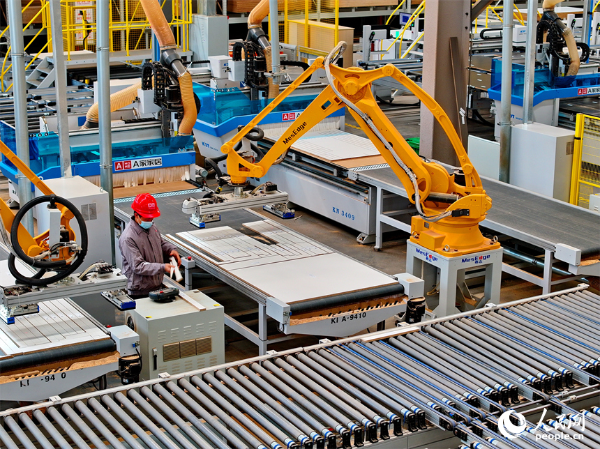 南康區的一家全屋定制家具生產企業智能制造車間內，工人在自動化生產線上調控智能機械臂加工板材。人民網 朱海鵬攝