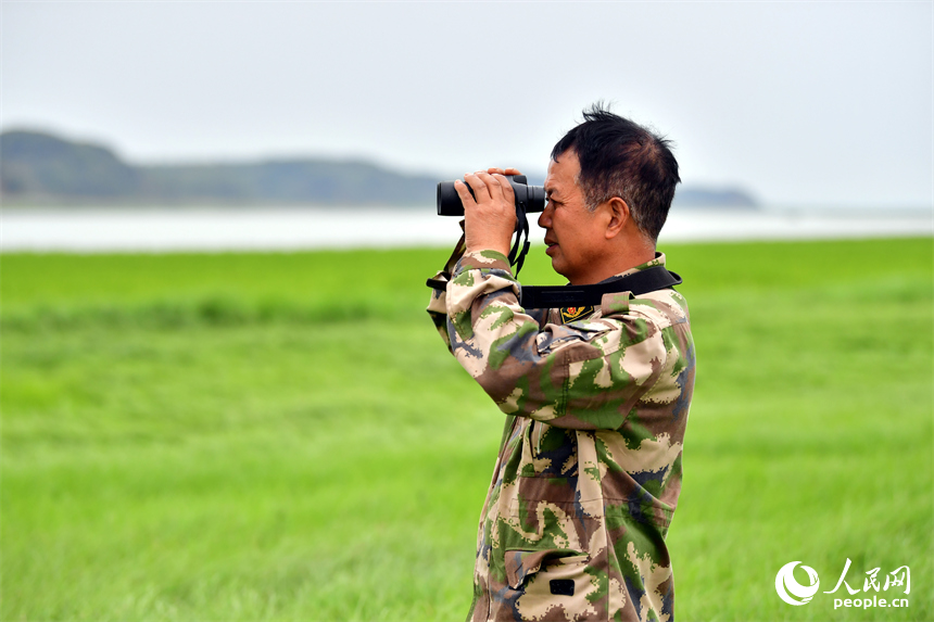 王小龍通過望遠鏡察看鄱陽湖湖面，觀察是否有落單候鳥。人民網記者 時雨攝