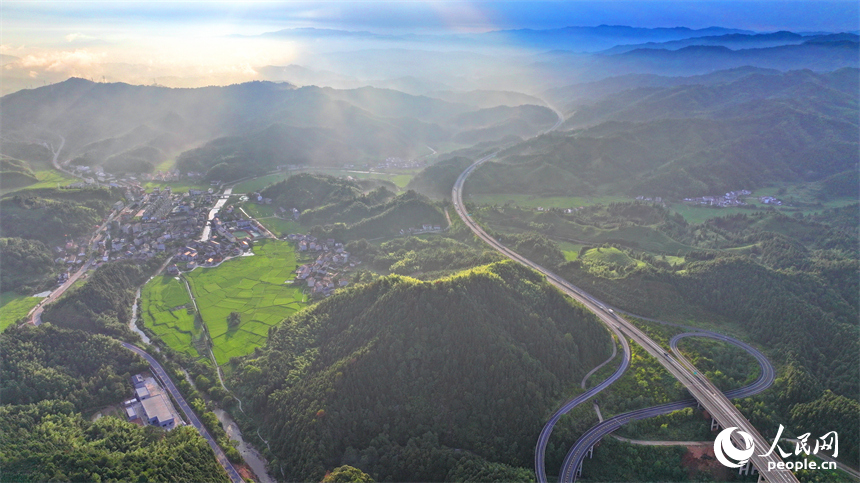 撫州市資溪縣嵩市鎮，撫（州）至吉（安）高速公路如同銀龍蜿蜒穿梭于蒼翠的崇山峻嶺間，與田園、村落相映成景。人民網 朱海鵬攝