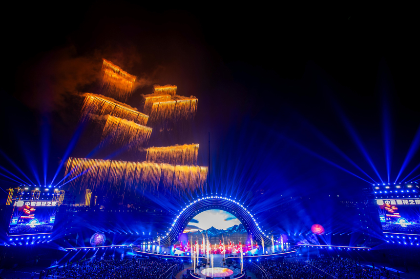 夜空綻放的絢爛煙花與下方燈火璀璨的舞臺、觀眾交相輝映。 顏紹明攝