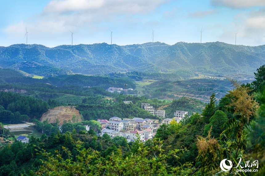 山脊上成片的風力發電機在青山綠樹間有序排布，與村落、山林構成和諧畫面。人民網 涂詩軒攝